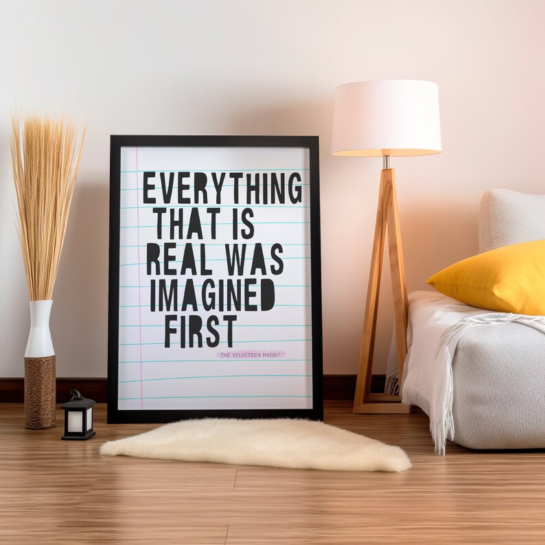 May include: Black framed poster with a white background and black text that reads "Everything that is real was imagined first." The text is on lined paper with blue lines. The poster is hanging on a white wall above a white rug.