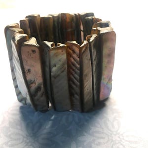 Könnte beinhalten: Ein Armband aus irisierenden, rechteckigen Muschelstücken. Das Armband ist übereinander gestapelt und hat einen natürlichen, organischen Look.