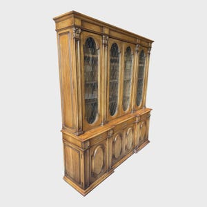 May include: A large, wooden display cabinet with glass-paned doors and decorative detailing. The cabinet has multiple sections, including upper glass-fronted doors and lower solid wood panels. The wood has a warm, natural finish, and the design is traditional.