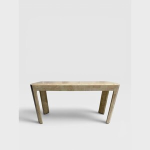 May include: A rectangular bench featuring a light beige, multi-tonal tiled surface with a visible grid pattern. The furniture piece has four sturdy, slightly angled legs that provide support, creating a clean and structured appearance.
