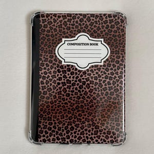 以下が含まれることがあります： 茶色と黒のヒョウ柄模様の、タブレットまたは電子書籍リーダー用の透明な保護ケースです。「COMPOSITION BOOK」と書かれた白いラベルと黒い背表紙が付いています。