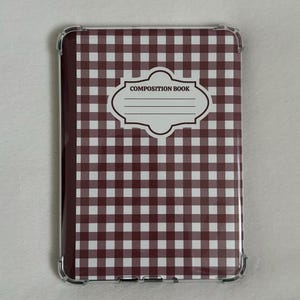 Puede incluir: Un cuaderno de composición con una funda transparente. La cubierta presenta un patrón de cuadros marrones y blancos. Una etiqueta blanca con las palabras "COMPOSITION BOOK" está centrada en la cubierta.