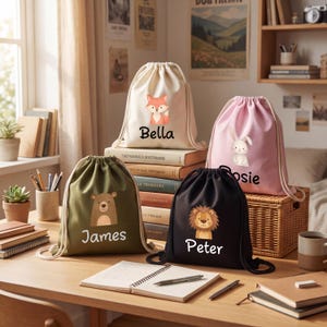Op de afbeelding: Vier trekkoordtassen in crème, roze, olijfgroen en zwart. Elke tas heeft een andere dierlijke afbeelding: een vos, een konijn, een beer en een leeuw. De namen "Bella", "Rosie", "James" en "Peter" staan eronder.