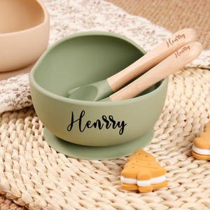 May include: A green silicone bowl with a suction base and two wooden spoons. The bowl and spoons are personalized with the name "Henry".