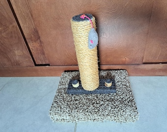 May include: A cat scratching post with a sisal-wrapped column, a gray plush base, and a dangling toy mouse. The column is tan, the base is gray and brown, and the toy mouse is gray with pink accents.