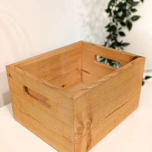 May include: A natural wood storage box with two cut-out handles on the sides. The box is empty and ready to be filled with items.