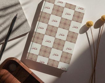 May include: A white notebook with a repeating pattern of brown and white geometric designs. The notebook has the Arabic word "فلسطين" (Palestine) printed in red on each square.