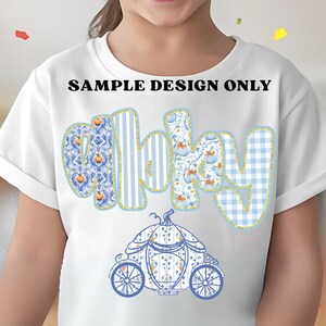 May include: White t-shirt featuring the word "baby" in blue and gold lettering with pumpkin and floral patterns. A blue and white carriage design is below the word. The text "SAMPLE DESIGN ONLY" is above the word.