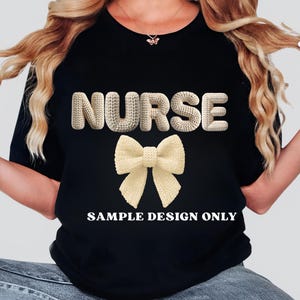May include: Black t-shirt with the word "NURSE" in a textured, off-white font above a matching bow. The text "SAMPLE DESIGN ONLY" is printed below the bow in a white, sans-serif font.