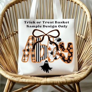 May include: White canvas tote bag with the text "Trick or Treat Basket Sample Design Only." The name "Abby" is displayed in orange and black Halloween-themed patterns, including spiders, pumpkins, and plaid. A black bow and ghost complete the design.