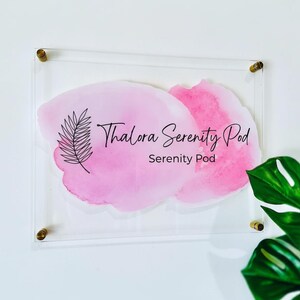 May include: Clear acrylic sign featuring the text "Thalora Serenity Pod" and "Serenity Pod" in black script over a pink watercolour design. The sign is mounted with gold-coloured hardware and a fern illustration.