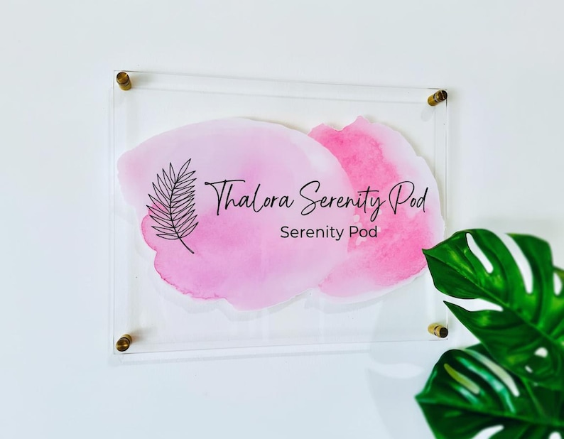 May include: Clear acrylic sign featuring the text "Thalora Serenity Pod" and "Serenity Pod" in black script over a pink watercolour design. The sign is mounted with gold-coloured hardware and a fern illustration.
