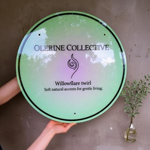 May include: A circular light green sign with a black border and black text that reads Olerine Collective, Willowflare twirl, and Soft natural accents for gentle living. A black spiral icon is centered between the brand name and text.