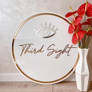 May include: A white circular sign with a gold border and the words "Third Sight" in gold script. A silver eye symbol is at the top. Red flowers in a white vase are to the right.