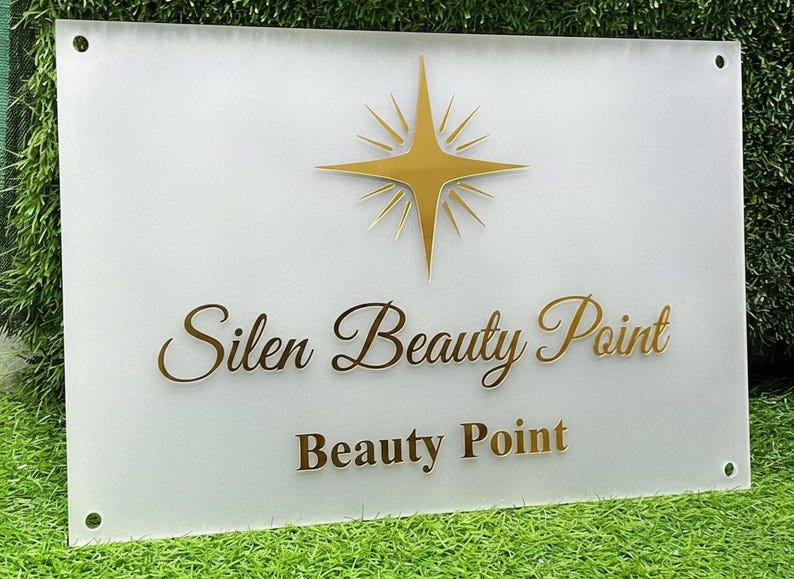 Może przedstawiać: Prostokątny znak z napisem "Silen Beauty Point" i "Beauty Point" złotymi literami. Złoty wz&oacute;r rozbłysku gwiazdy znajduje się na g&oacute;rze. Znak jest zamontowany na białym tle.