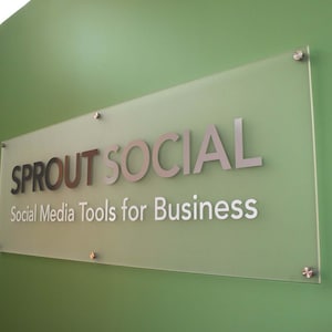 Pode incluir: Uma placa de vidro transparente com o texto "SPROUTSOCIAL" em letras prateadas e o slogan "Social Media Tools for Business" em letras brancas.