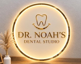 Può includere: Un'insegna da parete circolare con cornice in metallo dorato e retroilluminazione. L'insegna presenta un'icona a forma di dente dorato con un sorriso sottostante e il testo "DR. NOAH'S DENTAL STUDIO" in lettere dorate su sfondo circolare bianco sporco.