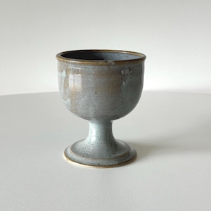 May include: A grey ceramic goblet with a brown rim. The goblet has a wide bowl and a short stem.
