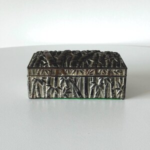 May include: A silver rectangular box with a raised design of bamboo stalks and leaves. The box has a green felt lining.