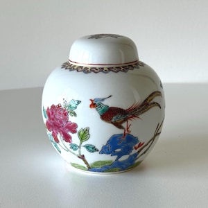 May include: A white porcelain jar with a lid, decorated with a colourful pheasant and floral design. The jar has a gold trim around the lid and base.