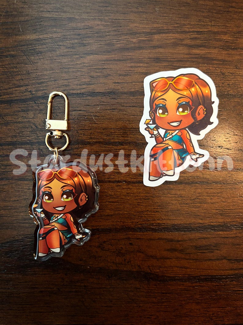 May include: A clear acrylic keychain and sticker featuring a cartoon character with tan skin, brown hair, and sunglasses. The character is wearing a blue top and orange bottoms, holding a cocktail. The keychain has a gold-colored clasp. The text "Stardustkinn" is visible.