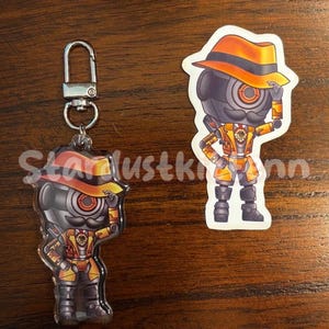 May include: Two robot-themed accessories: a keychain and a sticker. The keychain features a robot character with a hat and a mustache. The sticker shows the same robot character. Both have orange and yellow accents.