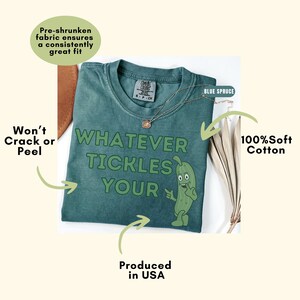 Peut inclure: Un t-shirt bleu &eacute;pic&eacute;a avec le texte "WHATEVER TICKLES YOUR" en lettres vert fonc&eacute; accompagn&eacute; d'un personnage de cornichon en dessin anim&eacute;. Le t-shirt pr&eacute;sente une &eacute;tiquette de marque Comfort Colors au col et est en coton 100% doux.