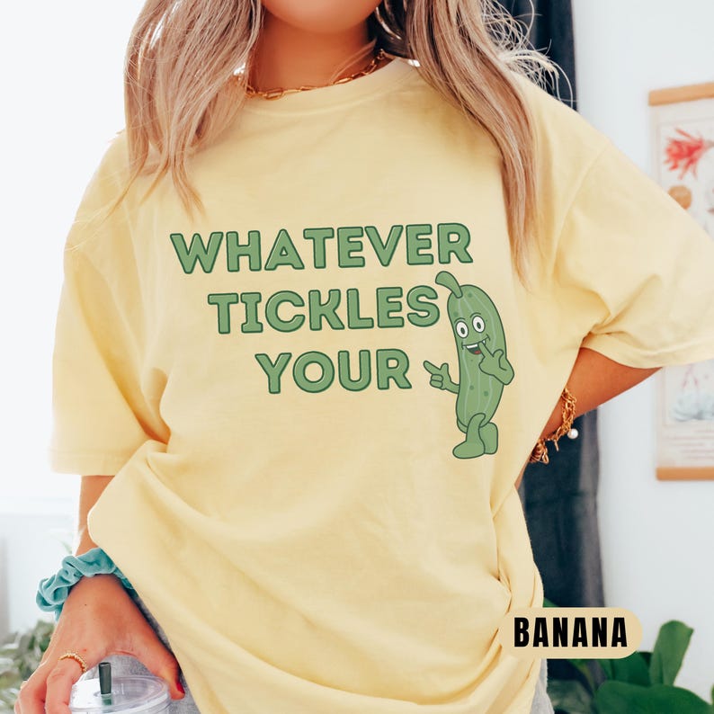 Woman wearing an banana Comfort Colors T-shirt featuring the phrase “Whatever Tickles Your Pickle” in green retro lettering with a cute illustrated pickle character beside the text. Casual unisex graphic tee shown styled with light denim for a fun pickle-themed shirt design.