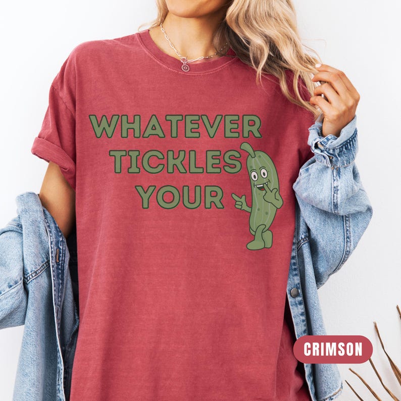 Woman wearing an crimson Comfort Colors T-shirt featuring the phrase “Whatever Tickles Your Pickle” in green retro lettering with a cute illustrated pickle character beside the text. Casual unisex graphic tee shown styled with light denim for a fun pickle-themed shirt design.