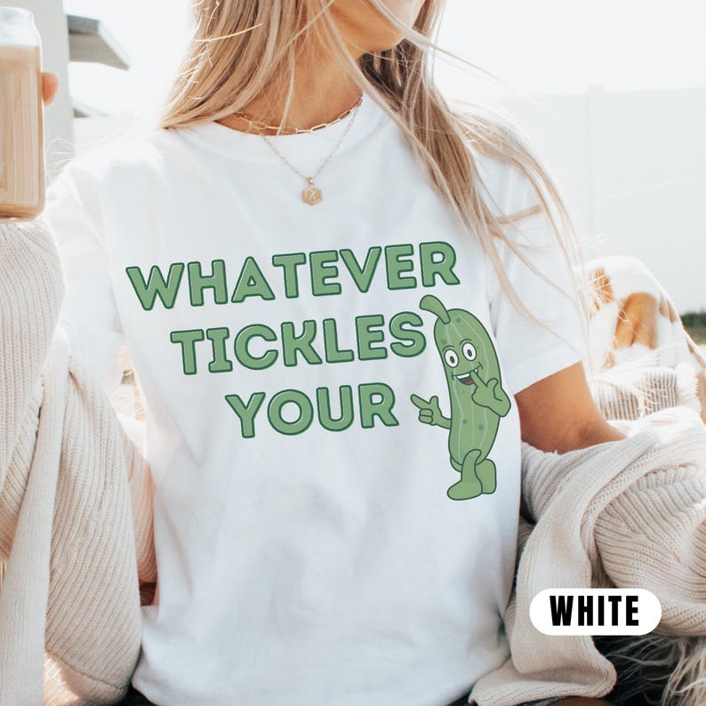Woman wearing an white Comfort Colors T-shirt featuring the phrase “Whatever Tickles Your Pickle” in green retro lettering with a cute illustrated pickle character beside the text. Casual unisex graphic tee shown styled with light denim for a fun pickle-themed shirt design.