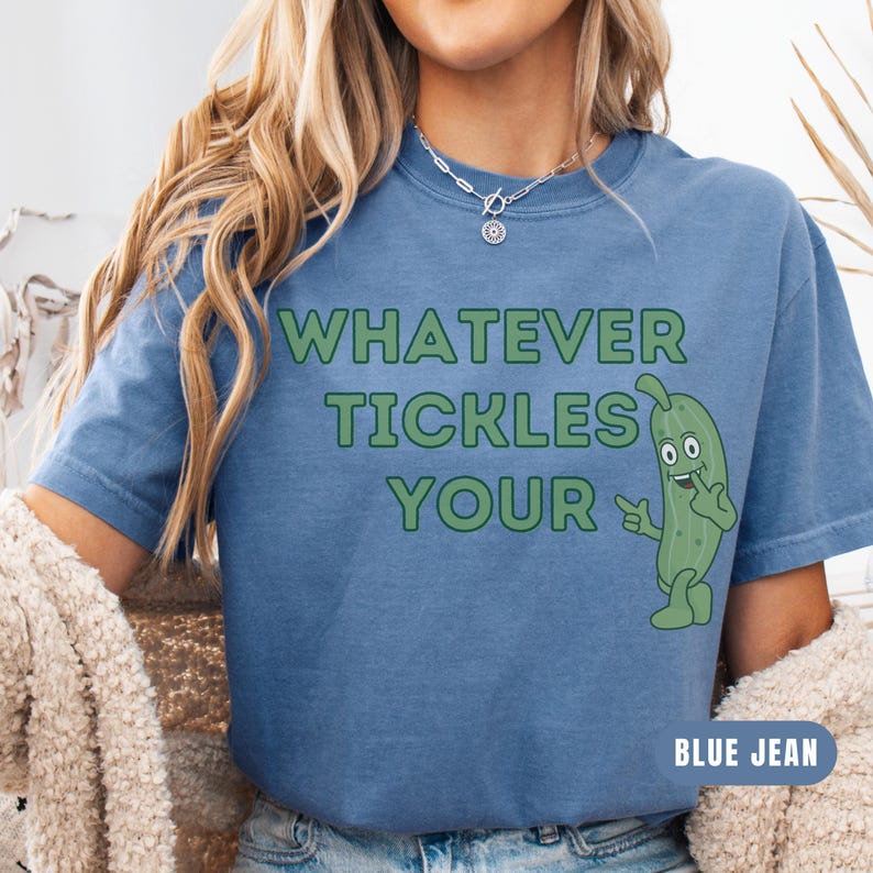 Woman wearing an blue jean Comfort Colors T-shirt featuring the phrase “Whatever Tickles Your Pickle” in green retro lettering with a cute illustrated pickle character beside the text. Casual unisex graphic tee shown styled with light denim for a fun pickle-themed shirt design.