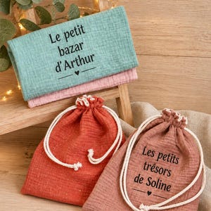 May include: Two drawstring pouches in rust and dusty pink, and a folded mint green cloth. The mint cloth features the text "Le petit bazar d'Arthur" with a heart icon. The dusty pink pouch features the text "Les petits trésors de Soline" with a heart icon.