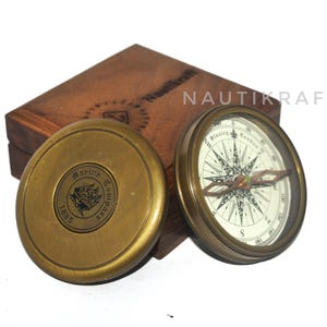May include: A vintage brass marine compass with a wooden box. The compass face features a detailed directional rose and the text "Stanley London". The lid of the compass case is engraved with "Marine Compass 1885". The wooden box is engraved with "Nautikraft".