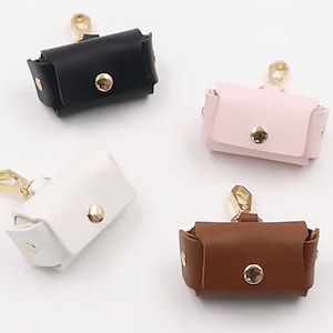 May include: Four leather cases for wireless earbuds in black, pink, white, and brown with gold clasps and a gold button.