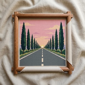 Può includere: Un ricamo a punto croce montato in una cornice di legno, raffigurante una strada dritta verso un tramonto. File di alti cipressi verde scuro fiancheggiano entrambi i lati della strada sotto un cielo rosa e arancione con nuvole.