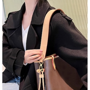 May include: A brown leather tote bag with a tan leather strap and gold hardware. The bag has a top zipper closure and a brown and tan patterned lining.
