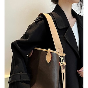May include: A brown leather tote bag with a tan leather strap and gold hardware. The bag has a top zipper closure and a small pocket on the front.