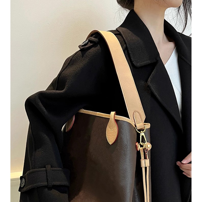 May include: A brown leather tote bag with a tan leather strap and gold hardware. The bag has a top zipper closure and a small pocket on the front.