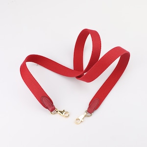 May include: Red canvas shoulder strap with gold metal clasps. The strap is designed for a handbag or purse.
