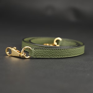 May include: A green leather strap with gold hardware. The strap is folded in half and the ends are connected with a gold clasp.