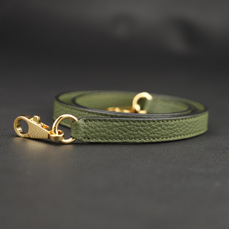 May include: A green leather strap with gold hardware. The strap is folded in half and the ends are connected with a gold clasp.