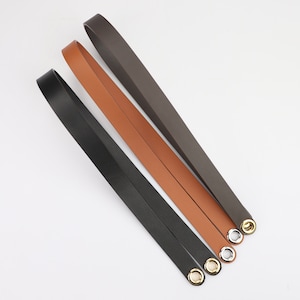 May include: Three leather straps in brown, black, and dark brown with silver eyelets. The straps are laid out in a diagonal pattern on a white surface.