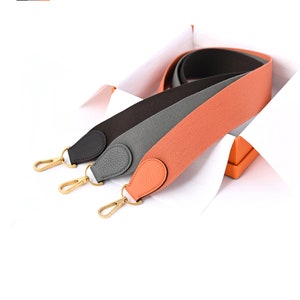 May include: Three leather straps in a box, one orange, one gray, and one black. Each strap has a gold metal clasp.