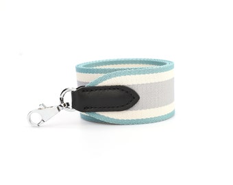 May include: A light blue and white striped fabric strap with a black leather accent and a silver hook.