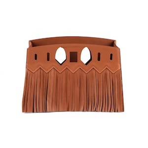Puede incluir: Una solapa de bolso de mano de cuero marrón claro con un diseño de flecos. La solapa presenta formas geométricas recortadas y un borde en zigzag. La flecos cuelgan del borde inferior de la solapa.