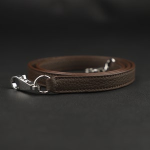 May include: A brown leather strap with a silver clasp. The strap is folded in half and the clasp is at the end of the strap.