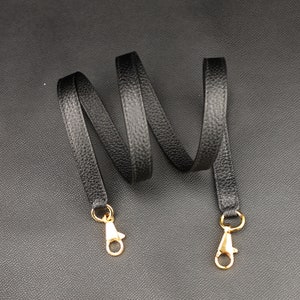 May include: Black leather strap with gold metal clasps. The strap is about 1.5 inches wide and is coiled on a black surface.