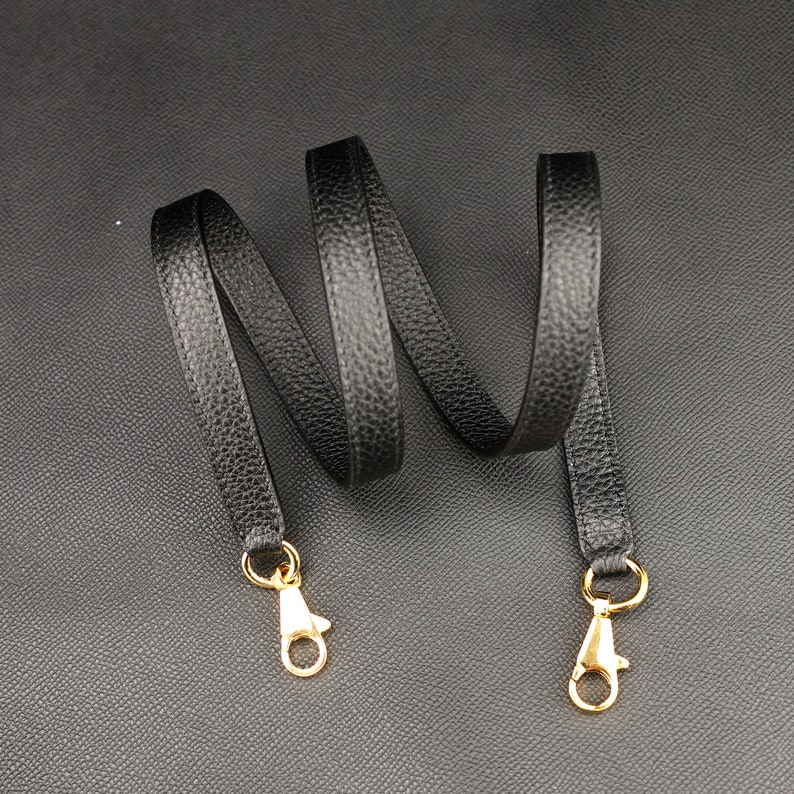 May include: Black leather strap with gold metal clasps. The strap is about 1.5 inches wide and is coiled on a black surface.