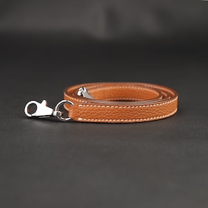 May include: A brown leather strap with a silver hook. The strap is folded in half and the hook is at the end of the strap.