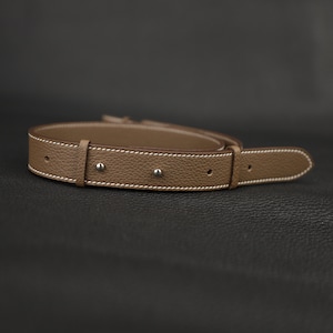 Peut inclure: Une ceinture en cuir marron avec des coutures blanches et des rivets argent&eacute;s.